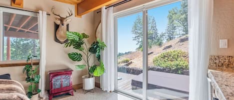 Habitación con techo de madera, cabeza de venado montada, estufa roja y vista a una ladera a través de amplios puertas correderas de vidrio.