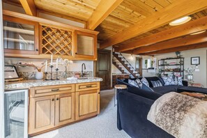 A spacious living area with a large black sofa, wooden cabinets, and a kitchen area with granite countertops. - Hot Tub + Scenic Views: Luxury Twain Harte Cabin! (Twain Harte)