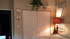A bedroom with a bed, a ceiling fan, a nightstand with a lamp, a plant, and a door. - Peaceful Paridise (Sarasota)