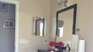 A bathroom with a wooden vanity, a large mirror, a towel rack, and a small table. - Peaceful Paridise (Sarasota)