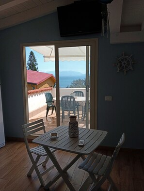 A room with a table and chairs, a TV mounted on the wall, and a view of the sea through a sliding door. - Apartment with sea view (Santa Flavia)