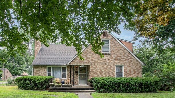 A brick house with a front porch, a small garden, and a pathway leading to the entrance.
