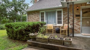 A brick house with a porch, two chairs, and planters.