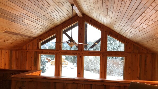 Une cabane chaleureuse avec un plafond en pente, une grande fenêtre et un ventilateur de plafond.