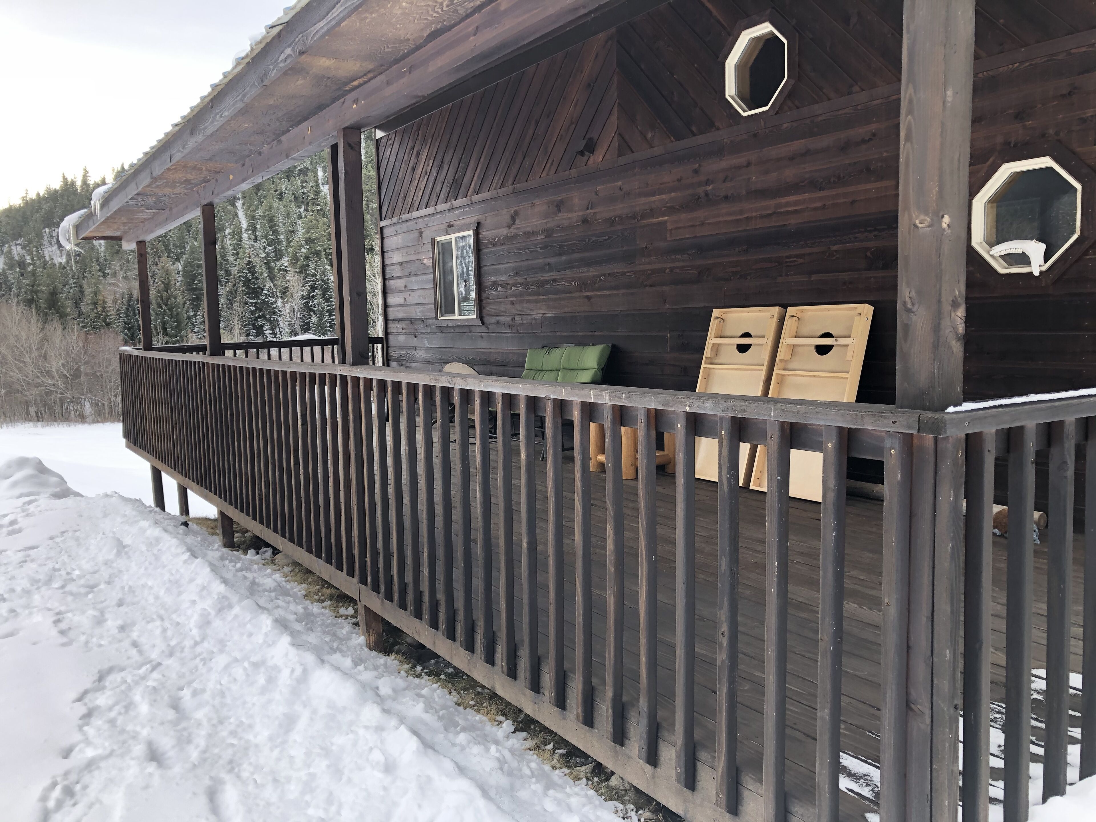 Une cabane en bois dotée d’un porche abrité et d’une terrasse recouverte de neige.