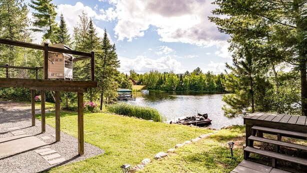 Una baita sul lago con una veranda in legno, un piccolo deposito e una barca ormeggiata.