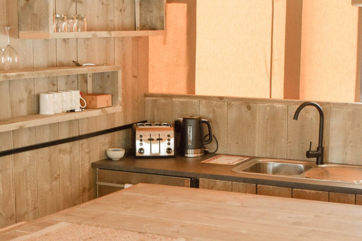 A kitchen with wooden walls, a table, chairs, a toaster, a kettle, and a sink.