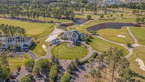 Vue aérienne d’un terrain de golf avec un club-house, des aires de stationnement et la végétation environnante.