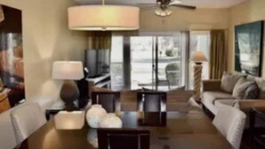 Une chambre d’hôtel moderne dotée d’un coin repas, d’un canapé, d’une télévision et d’un ventilateur de plafond.