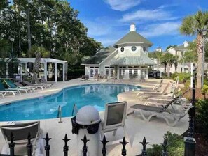Relax by the pool surrounded by lounge chairs and umbrellas, with a gazebo nearby and a building in the background.