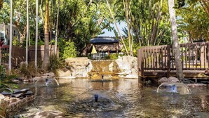 A tranquil outdoor setting with a pond, wooden deck, and a thatched-roof structure.