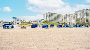 Une plage avec des parasols bleus et des chaises longues, et des immeubles de grande hauteur en arrière-plan.