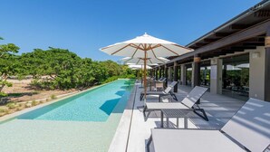 A poolside area with lounge chairs and umbrellas, surrounded by greenery and a clear sky. - PH Vista Encanto in El Encanto by Mita Residential. Golf & Ocean View, Pool, Golf Cart (Punta Mita)