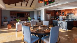 A spacious living area with a dining table, blue chairs, and a kitchen with wooden cabinets and modern appliances. - PH Vista Encanto in El Encanto by Mita Residential. Golf & Ocean View, Pool, Golf Cart (Punta Mita)