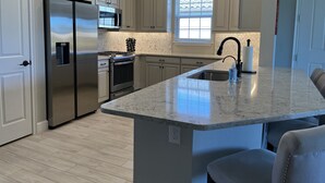 Een moderne keuken met witte kasten, roestvrijstalen apparatuur, een groot schiereiland met een spoelbak en een raam dat voor natuurlijk licht zorgt.