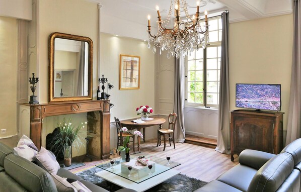 A living room with a fireplace, a chandelier, a television, and a dining area with a table and chairs. - 2 bedroom gorgeous apartment in Sarlat-la Canéda (Sarlat-la Canéda)