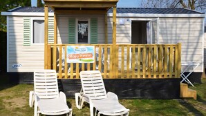 A mobile home with a deck, two white lounge chairs, and a 'Happy Premium' sign. - Mobilehome with air conditioning, terrace and pool (Carovigno)