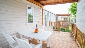 A covered outdoor patio with a white table and chairs, a bottle, and fruit. - Mobilehome with air conditioning, terrace and pool (Carovigno)