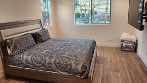 A bedroom with a large bed, two windows, a ceiling fan, and a TV mounted on the wall. - Madison's Place<br>Cozy & Comfortable Modern Home (Paramount)