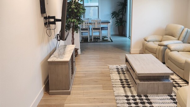 A modern living room with a wooden floor, a sofa, a coffee table, and a TV mounted on the wall. - Madison's Place<br>Cozy & Comfortable Modern Home (Paramount)