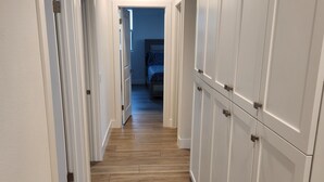 A hallway with wooden flooring, white walls, and a closet with multiple doors. - Madison's Place<br>Cozy & Comfortable Modern Home (Paramount)