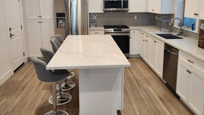 A modern kitchen with white cabinetry, stainless steel appliances, and a marble countertop. - Madison's Place<br>Cozy & Comfortable Modern Home (Paramount)