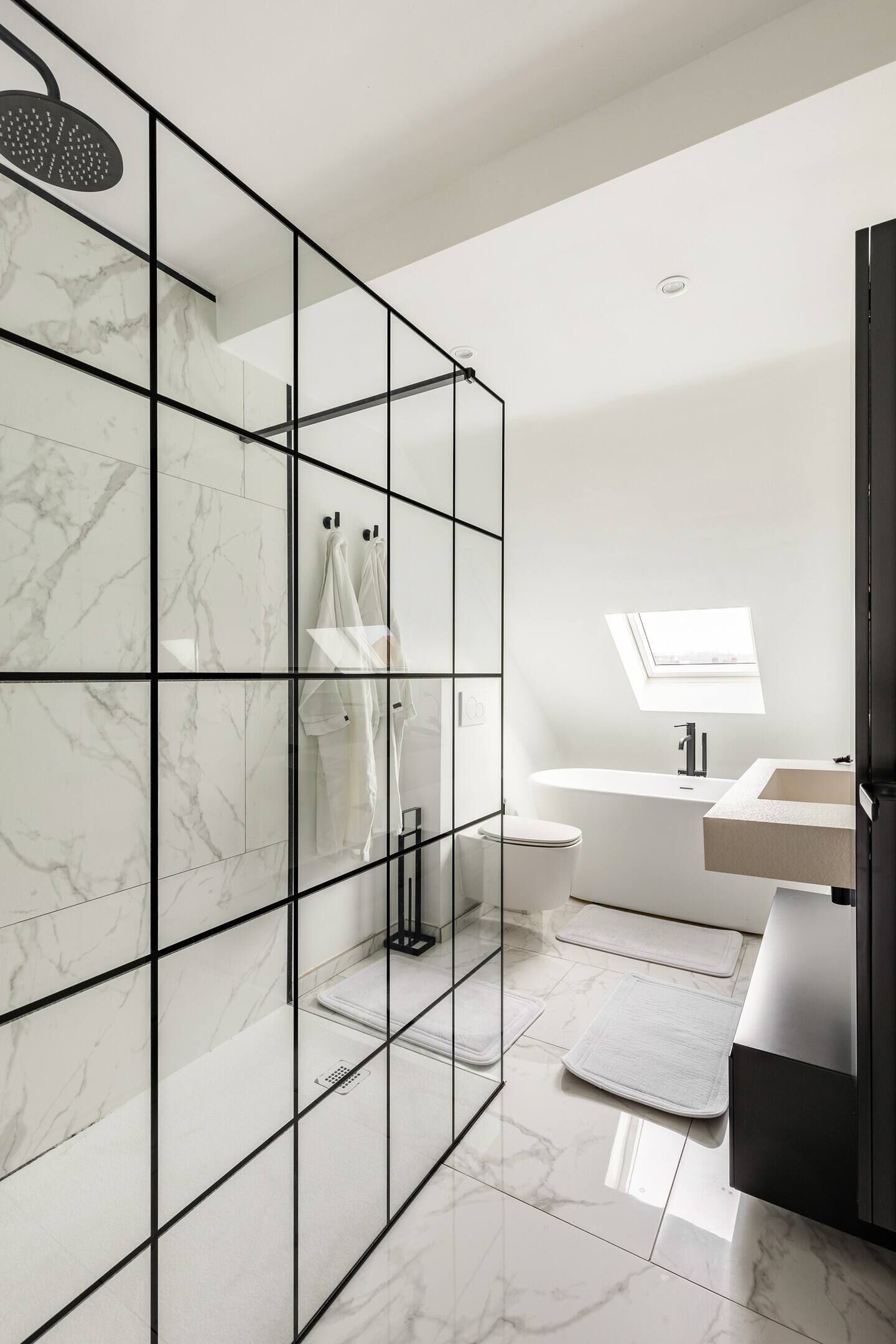 A modern bathroom with a glass-enclosed shower, a skylight, a white toilet, and a vanity with a mirror.