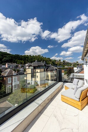 Une terrasse sur le toit dotée d’une balustrade en verre, d’un canapé en bois et offrant une vue sur le paysage urbain.