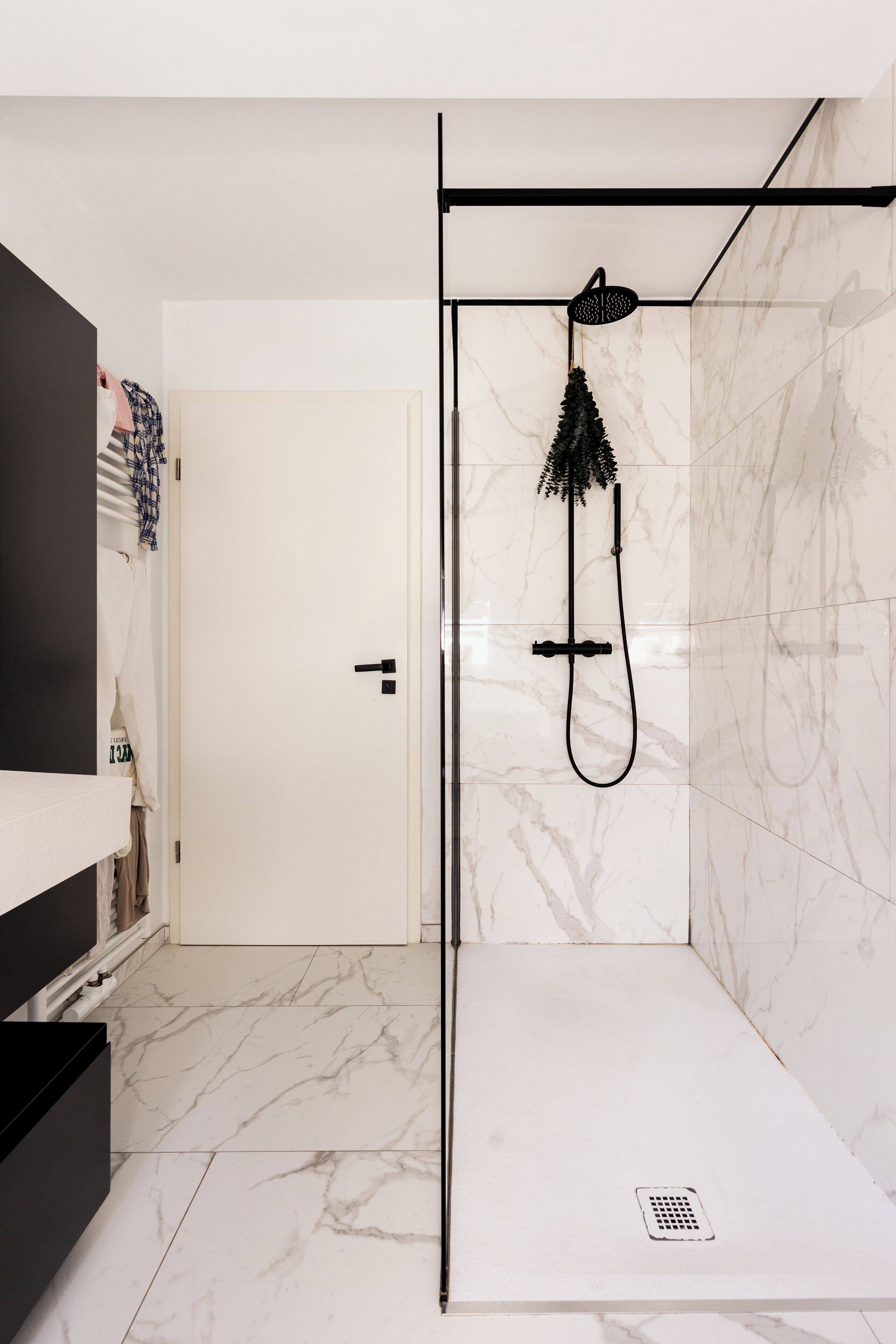 A modern bathroom with a shower, marble tiles, and a black door.