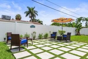 A patio with outdoor furniture, a striped umbrella, and a white fence.