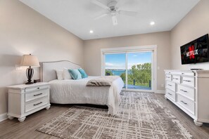 A bedroom with a bed, nightstand, dresser, TV, and a view of the outdoors. - 🌆 539 Bay St Lakeview Condo | Walk to Downtown & Beach (Traverse City)
