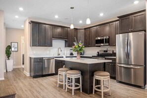 A modern kitchen with dark wood cabinets, stainless steel appliances, a central island with stools, and pendant lighting. - 🌆 539 Bay St Lakeview Condo | Walk to Downtown & Beach (Traverse City)