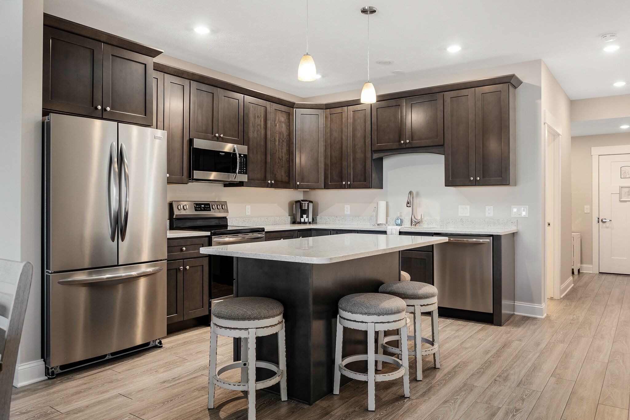 Dark wood kitchen cabinets, stainless appliances and a light island with three stools.