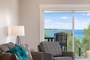 A room with a sofa, a chair, and a table. There is a view of the sea through a glass door. - 🌆 539 Bay Downtown Traverse City Lakeview Condo - Steps to Beach & Festival Grounds (Traverse City)