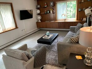 Relax in a spacious living room with a large window, flat-screen TV, and comfortable seating area.
