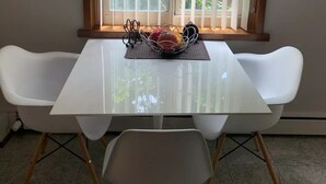 A dining area with a white table, two white chairs, a metal fruit basket, and a window with blinds. - Beautiful Modern Condo Downtown/Convention Center (Seattle)