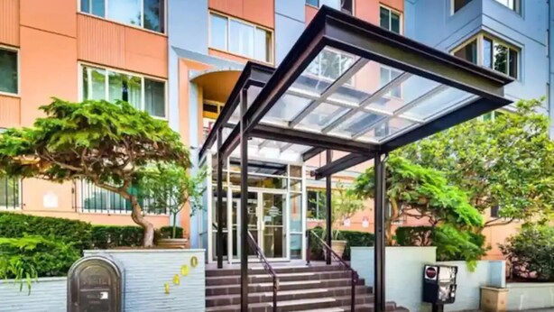 A modern building with a glass entrance, steps leading up to a covered area, and a mailbox on the sidewalk. - Beautiful Modern Condo Downtown/Convention Center (Seattle)