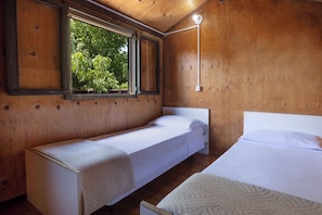 Une chambre avec deux lits, des murs en bois, une fenêtre donnant sur les arbres et un luminaire fixé au mur.