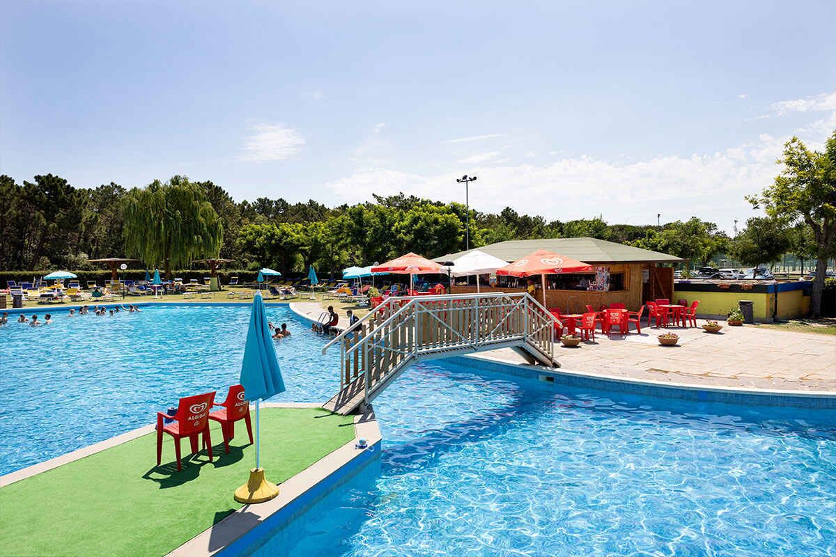A swimming pool with a bridge, red chairs, and umbrellas.