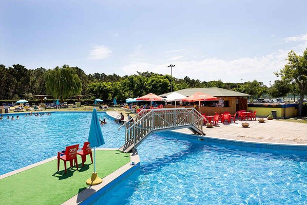 A swimming pool with a bridge, red chairs, and umbrellas.