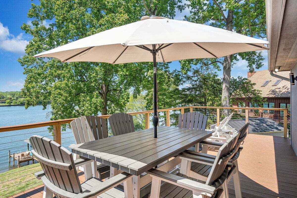 A deck with a table and chairs, overlooking a body of water and trees.