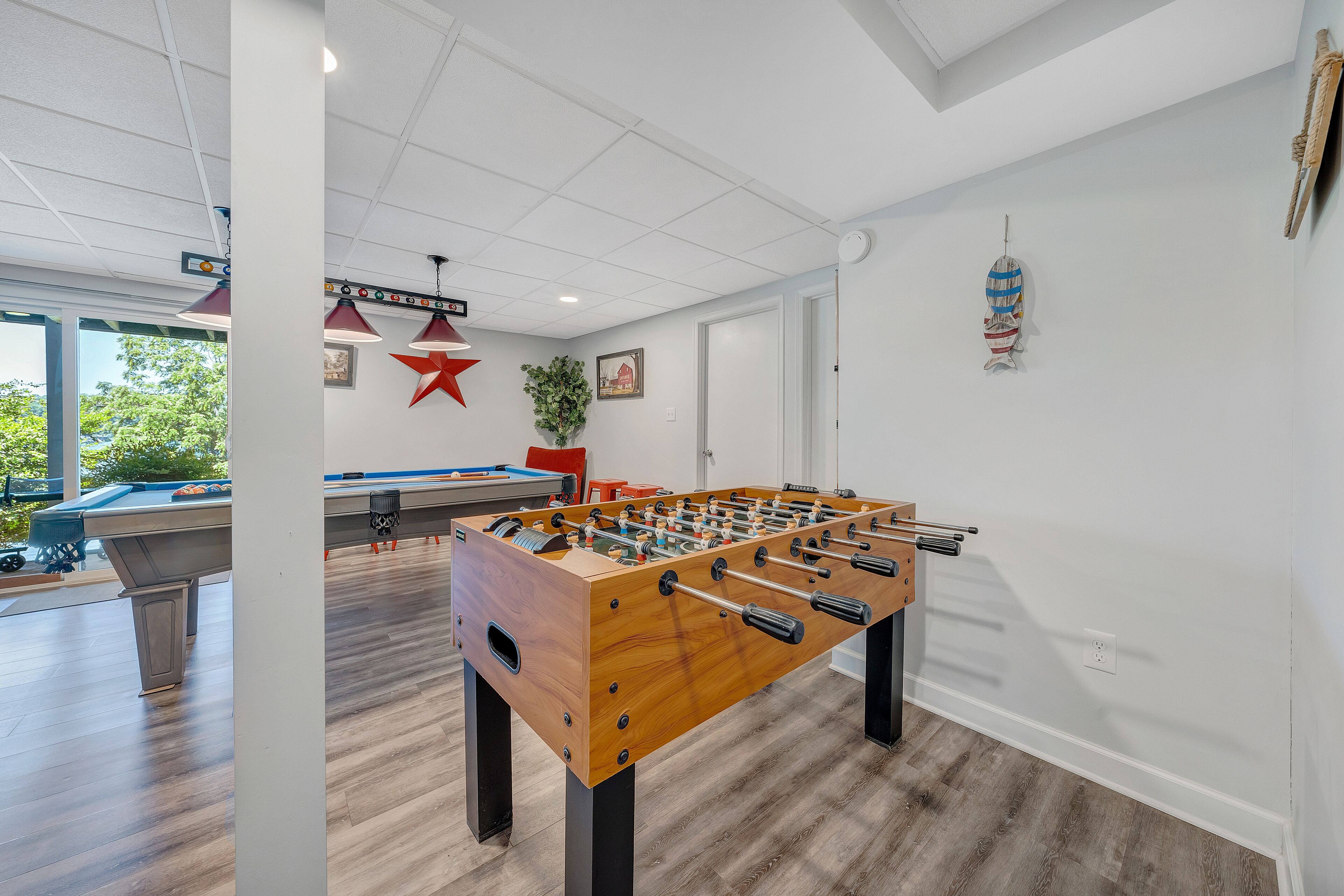 Ein Zimmer mit Tischfußball, Billardtisch und einem großen Fenster mit Blick auf Bäume.