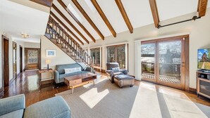 A spacious living area with a staircase, wooden beams, large windows, and a view of the outdoors. - Pine Knob Point - Lakehouse w/ Private Dock (Moneta)