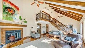 A spacious living room with a fireplace, a staircase, and a large painting. - Pine Knob Point - Lakehouse w/ Private Dock (Moneta)