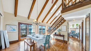 A spacious dining area with a wooden table and chairs, a chandelier, and a staircase leading to an upper level. - Pine Knob Point - Lakehouse w/ Private Dock (Moneta)