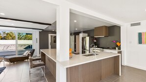 Eine moderne Küche mit einer zentralen Kochinsel, einem Essbereich mit Sofa und Stühlen sowie Blick ins Freie.