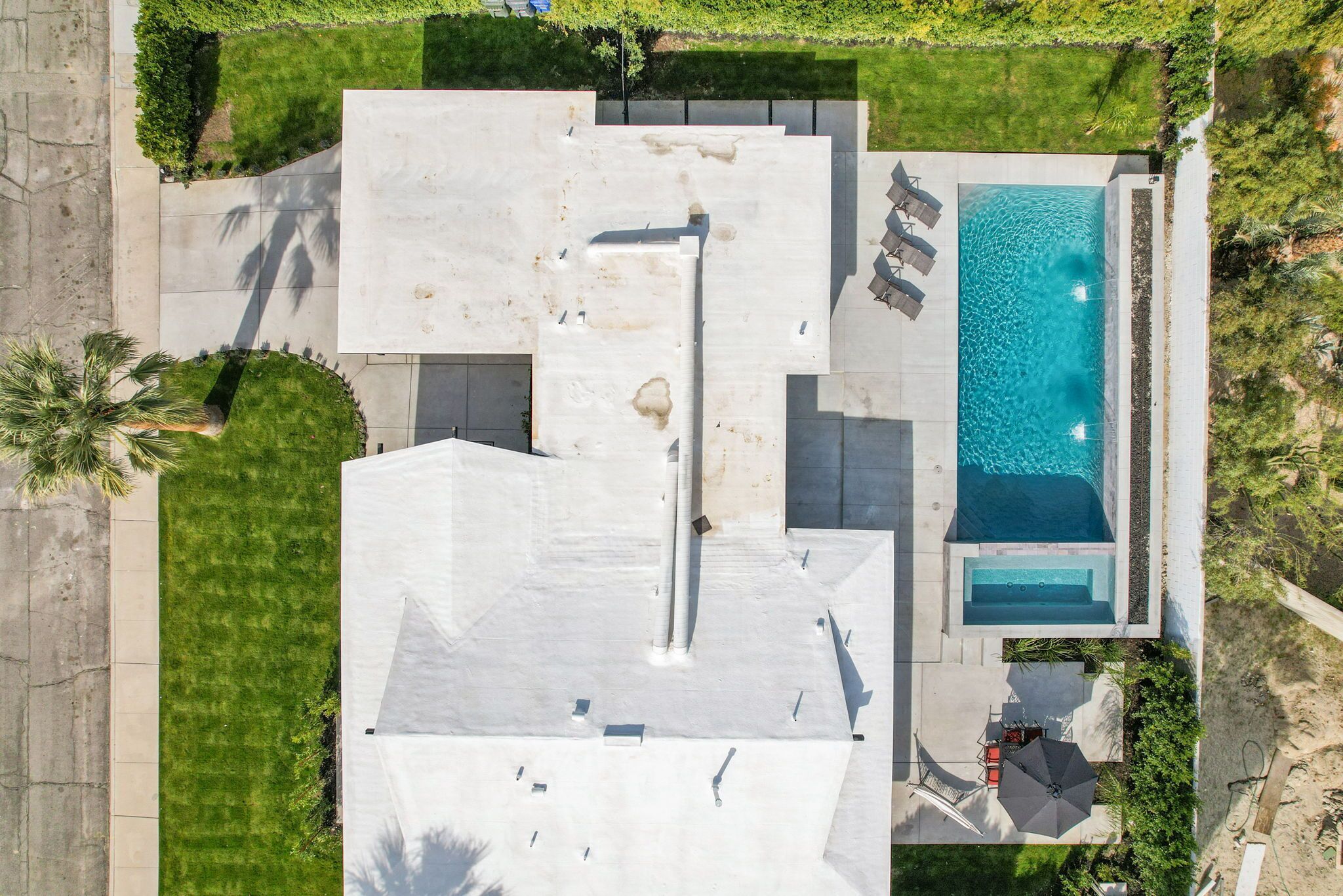 An aerial view of a property with a swimming pool, a covered patio, and a lawn.