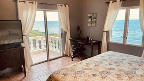 Une chambre avec un lit, un bureau, une chaise, une télévision et un balcon donnant sur la mer.
