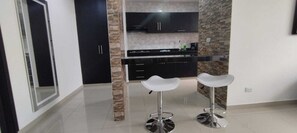 Une cuisine moderne avec des meubles noirs, un plan de travail en marbre et deux tabourets de bar blancs.
