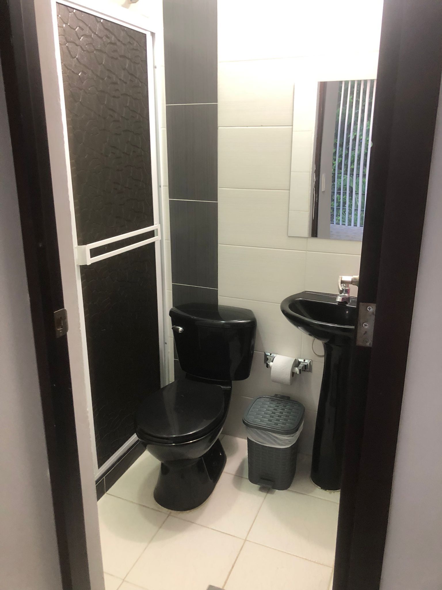 Une petite salle de bain avec des toilettes noires, un lavabo et une poubelle.